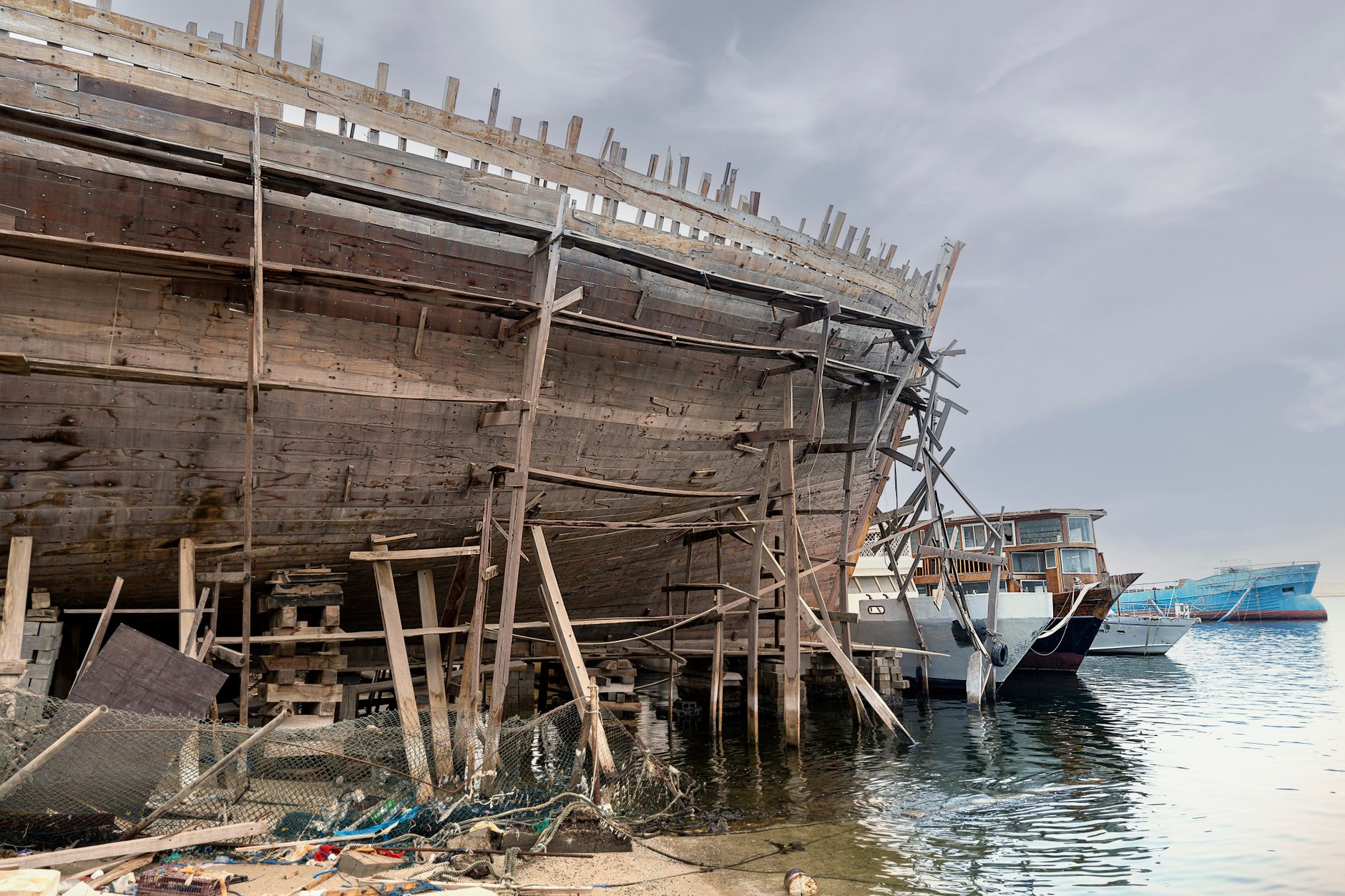 a modern destroyer under construction in a large covered shipyard dry dock, with scaffolding and cranes surrounding the hull
