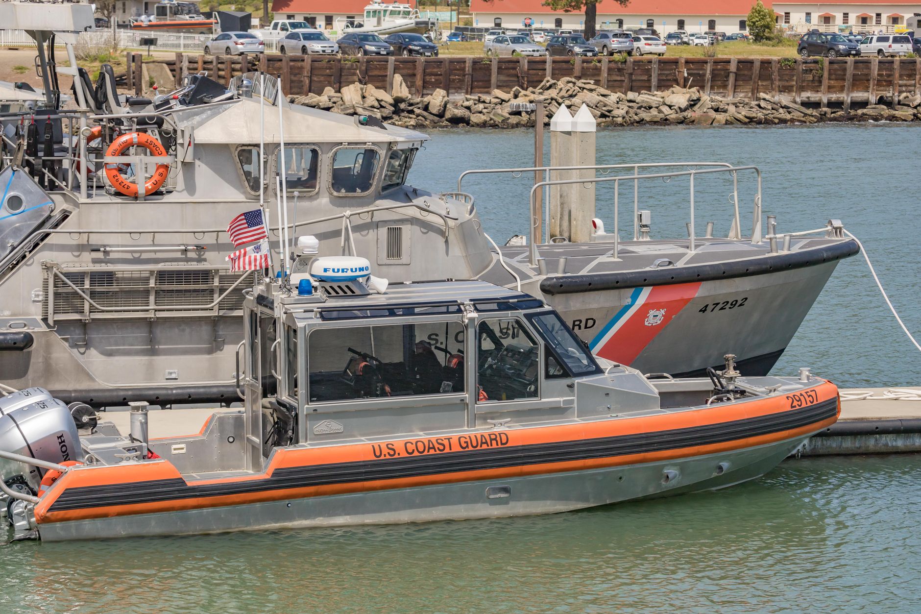 a coast guard operations facility along a river port, with small patrol craft visible at a concrete jetty in the background