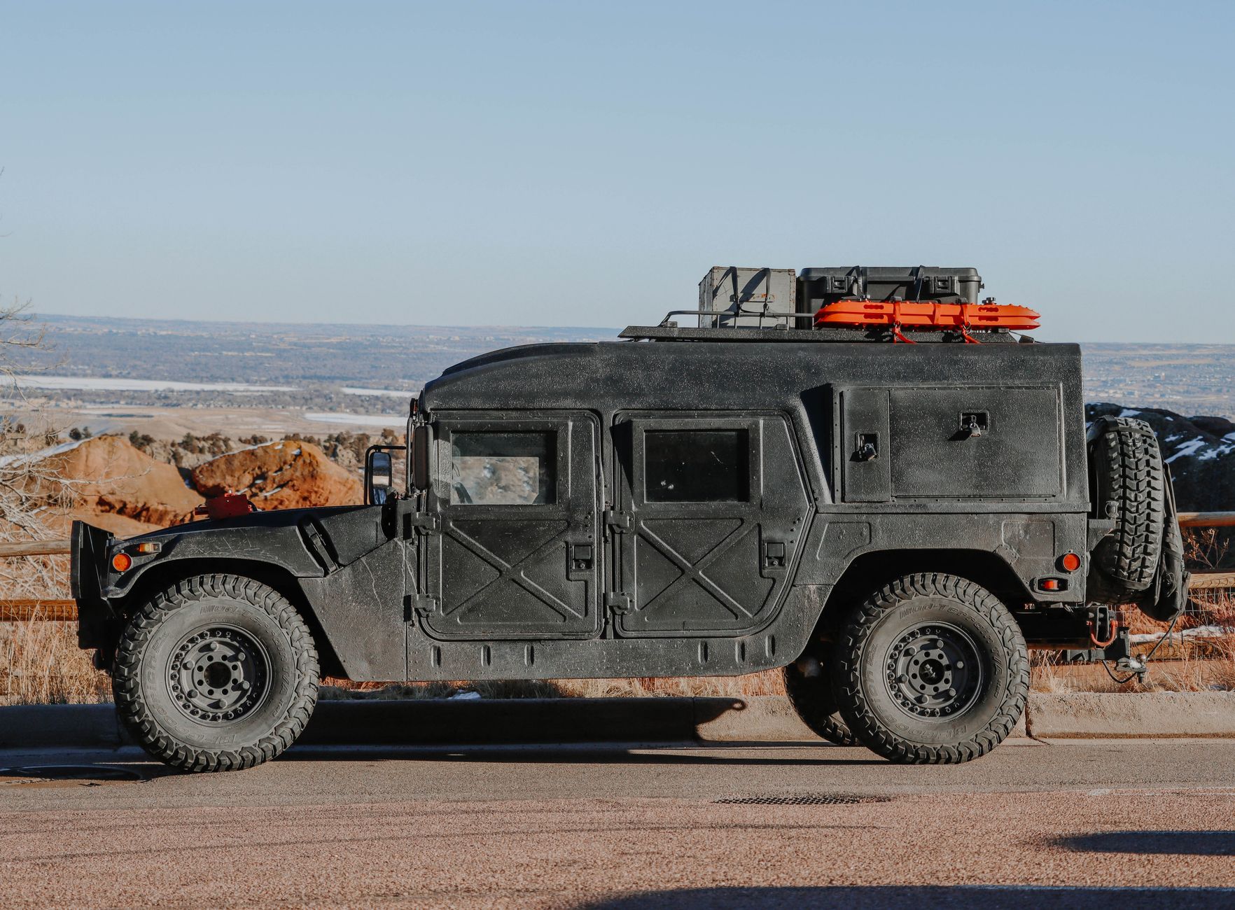 a row of wheeled armored personnel carriers parked on a desert military base, viewed from a wide angle showing the full vehicle line and surrounding hardened storage facilities