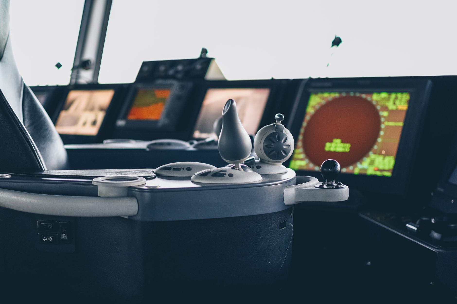interior of a naval vessel operations room showing navigation consoles and radar displays, with ambient lighting from multiple screens illuminating the space