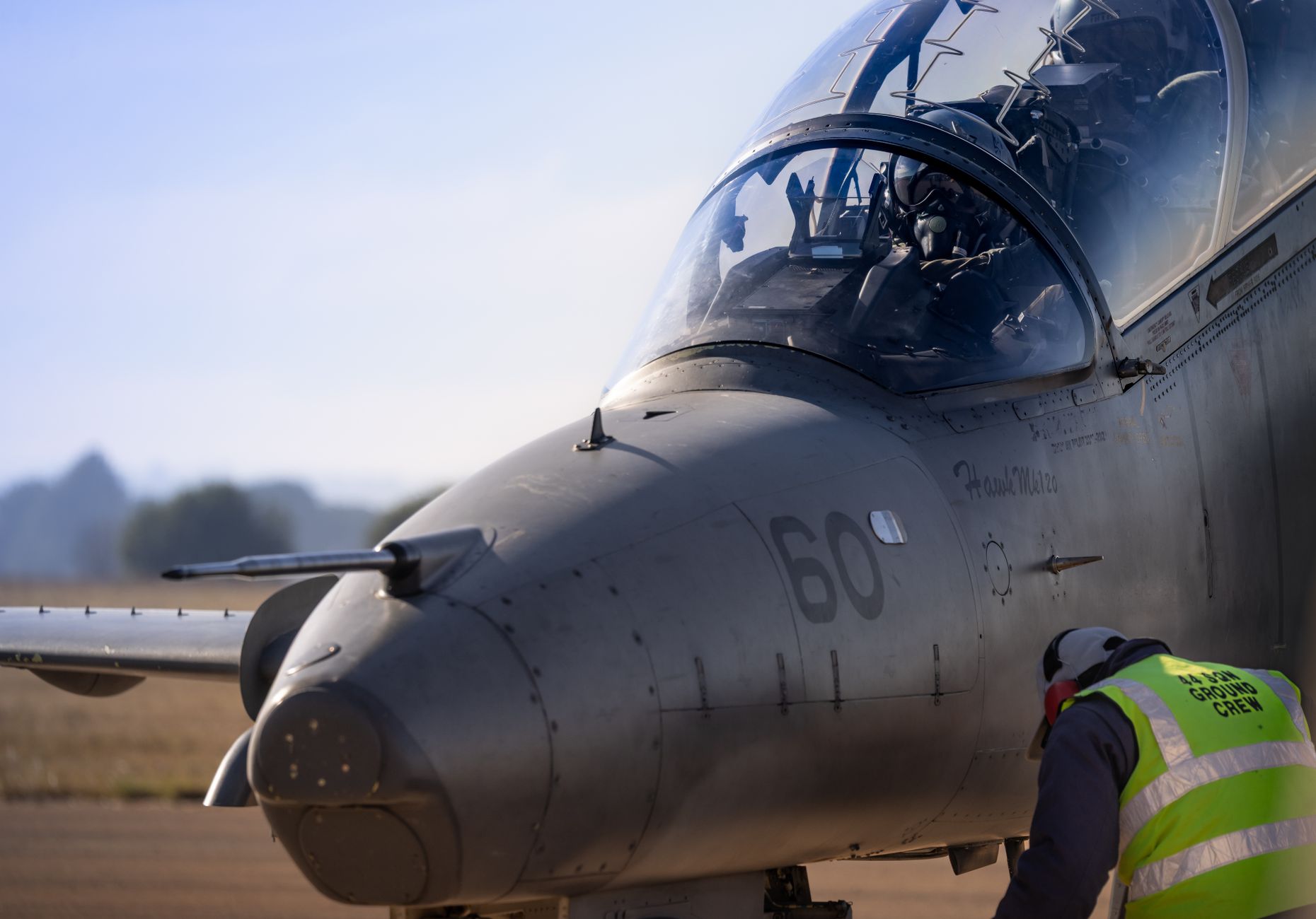 a T-45 Goshawk trainer jet parked on a naval air station flight line, engines visible, ground equipment nearby