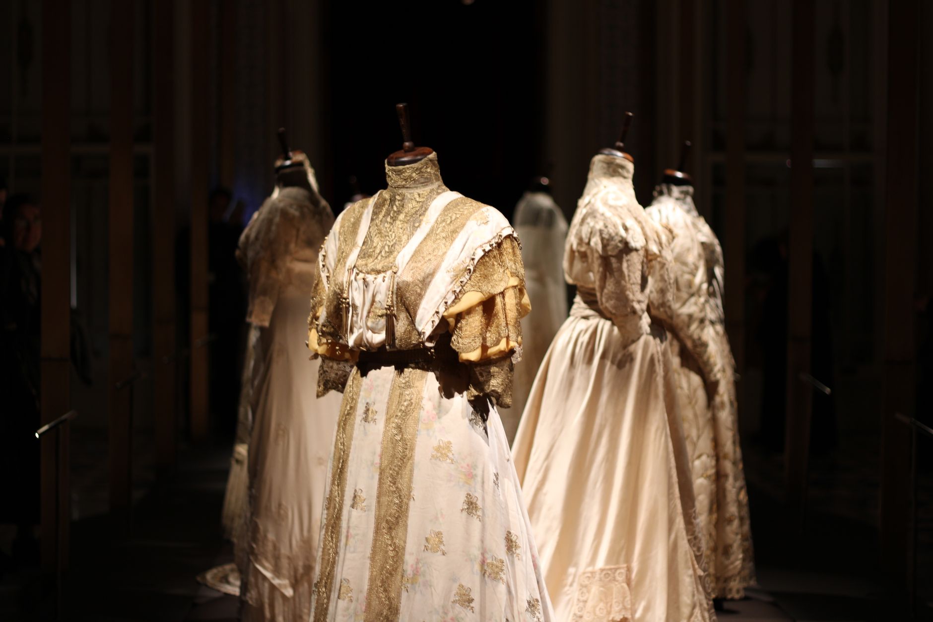a wide interior hall of a modern presidential museum, display cases lining the walls with formal garments mounted on mannequins under warm exhibition lighting