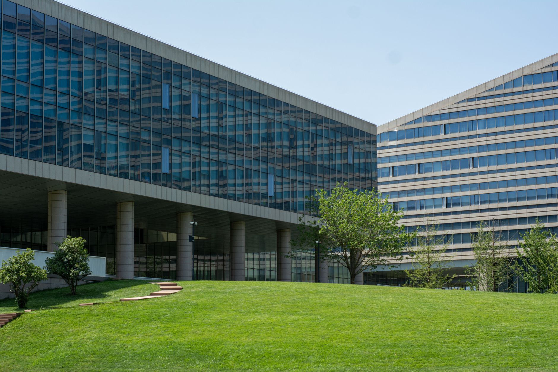 a large corporate campus building with glass facades reflecting an overcast sky, surrounded by manicured grounds and empty parking structures, viewed from street level