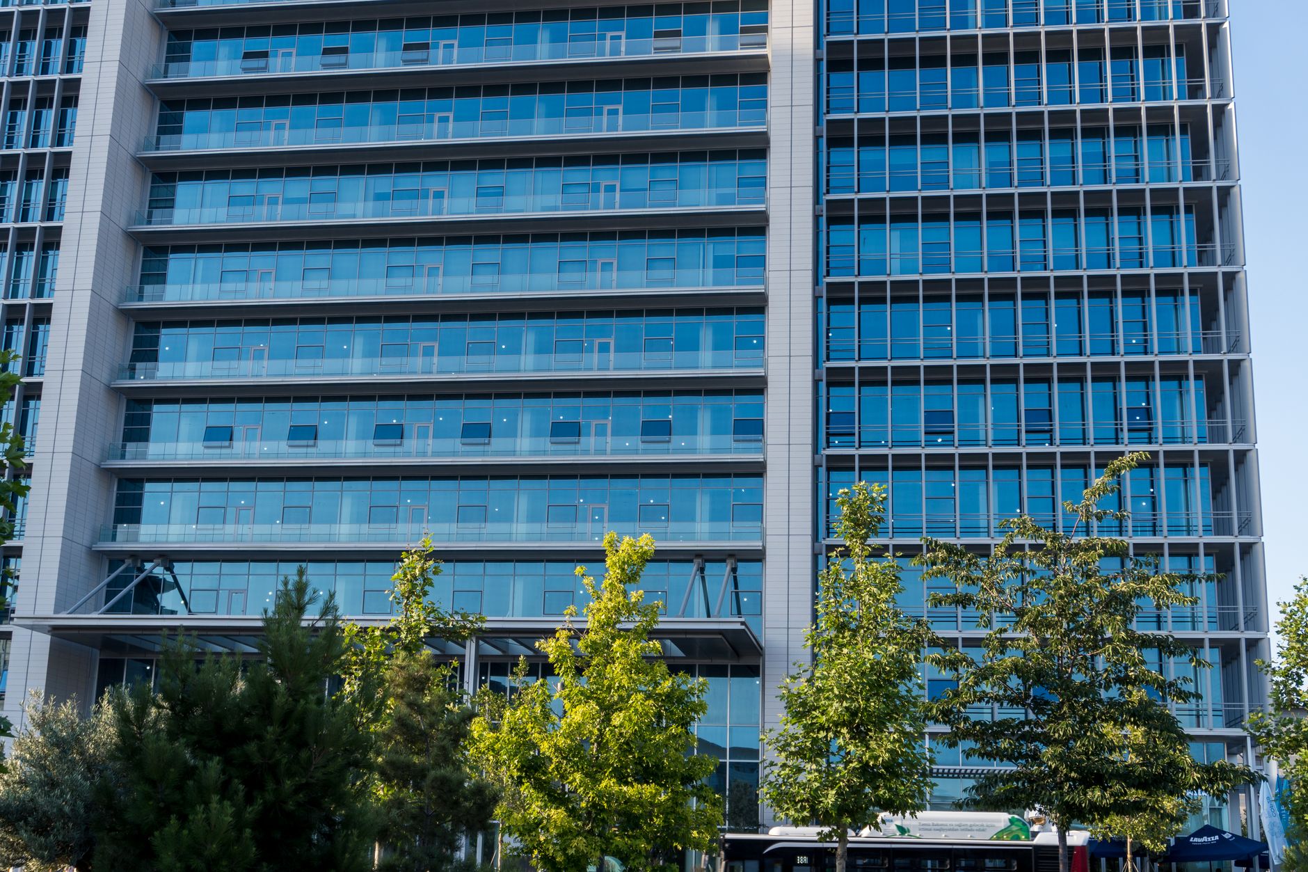 an exterior view of a corporate technology campus with a glass-fronted office building, empty parking structure visible in the background, and a clear sky overhead