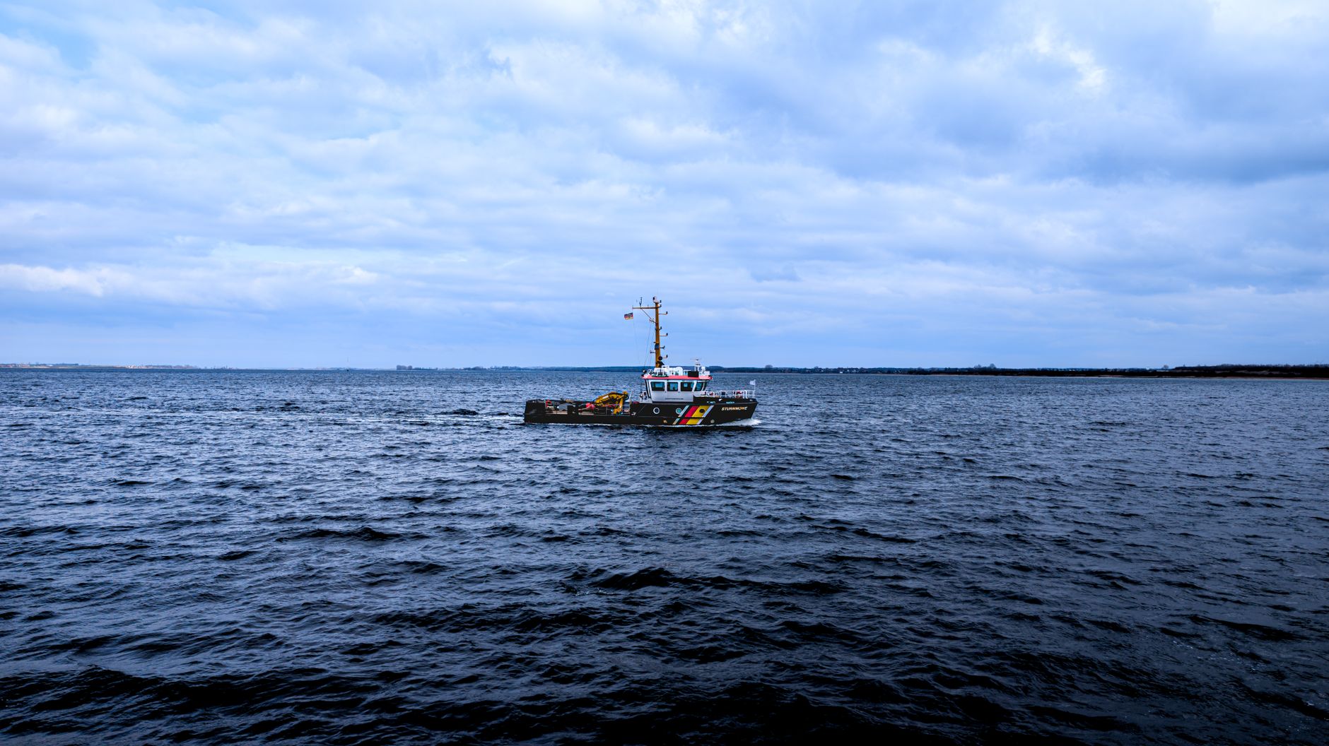 a compact naval patrol vessel underway in gray Baltic Sea conditions, viewed from a low angle at the waterline with overcast skies