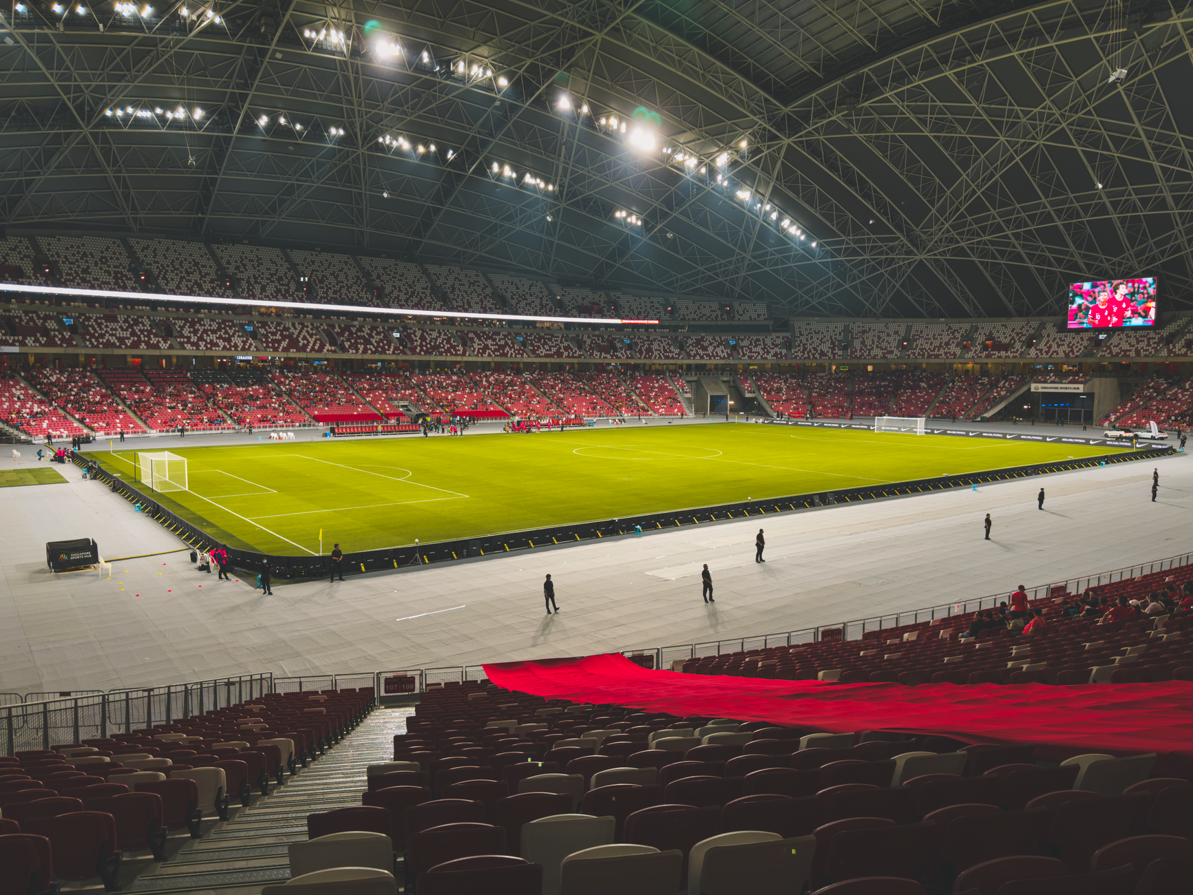 an empty professional football stadium interior with the field turf visible, overhead stadium lights illuminating the field before a game, sideline equipment carts in the background