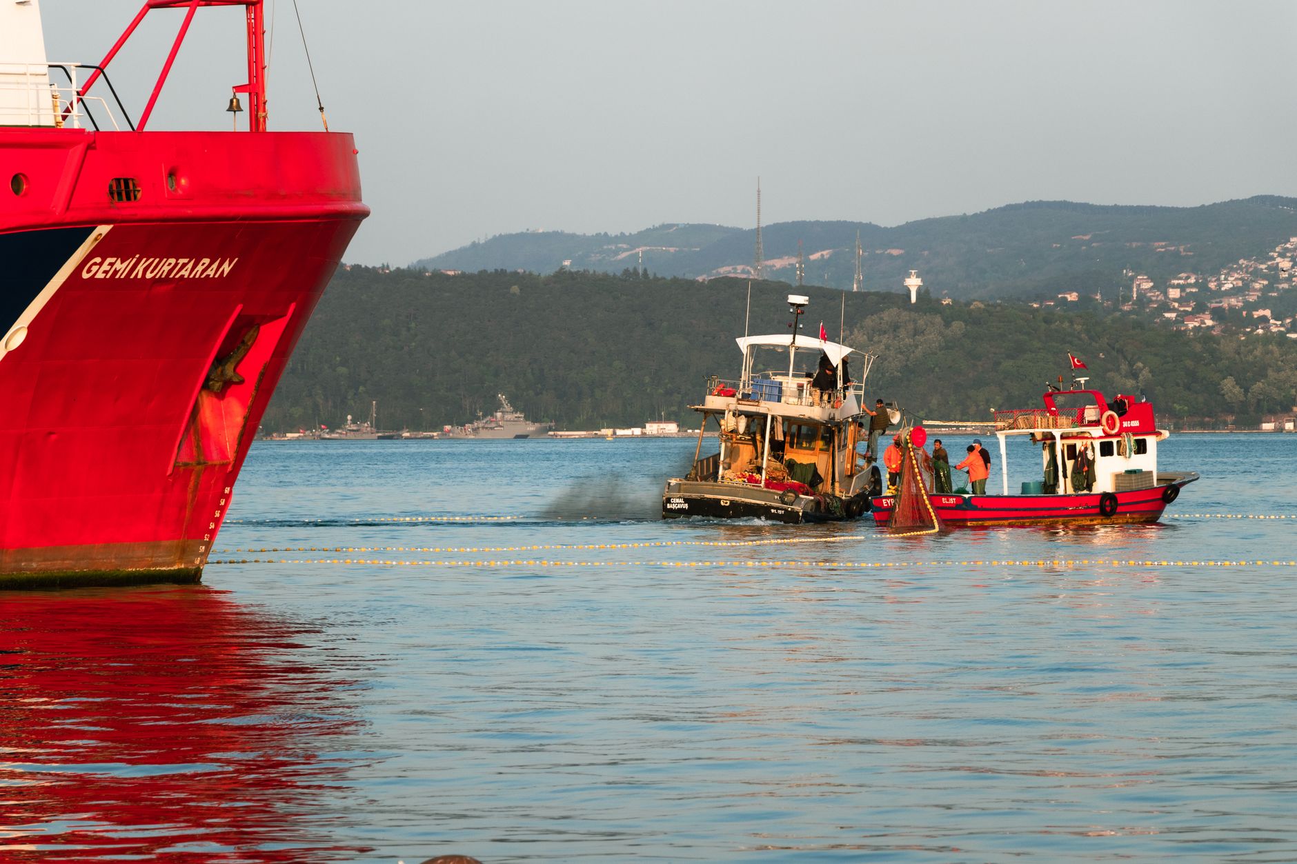 An unmanned underwater vehicle being recovered onto the rear deck of a mine countermeasures vessel at sea, with crew members visible at a distance in the background