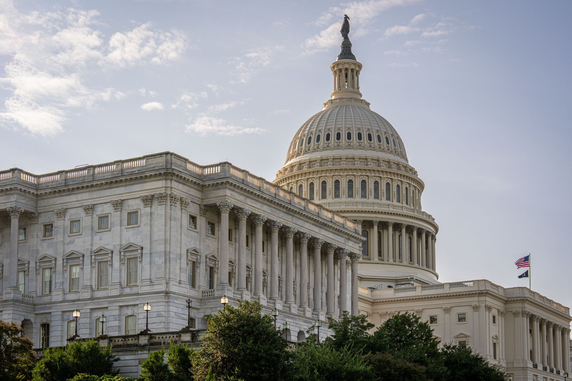 a wide-angle view of the US Capitol building exterior on a clear day, American flags visible along the facade, no people in foreground