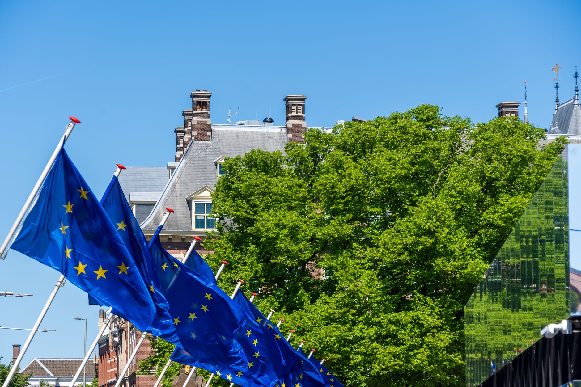 an exterior view of NATO headquarters in Brussels, the alliance flag and member-nation flags mounted along an entrance plaza, building architecture visible in background