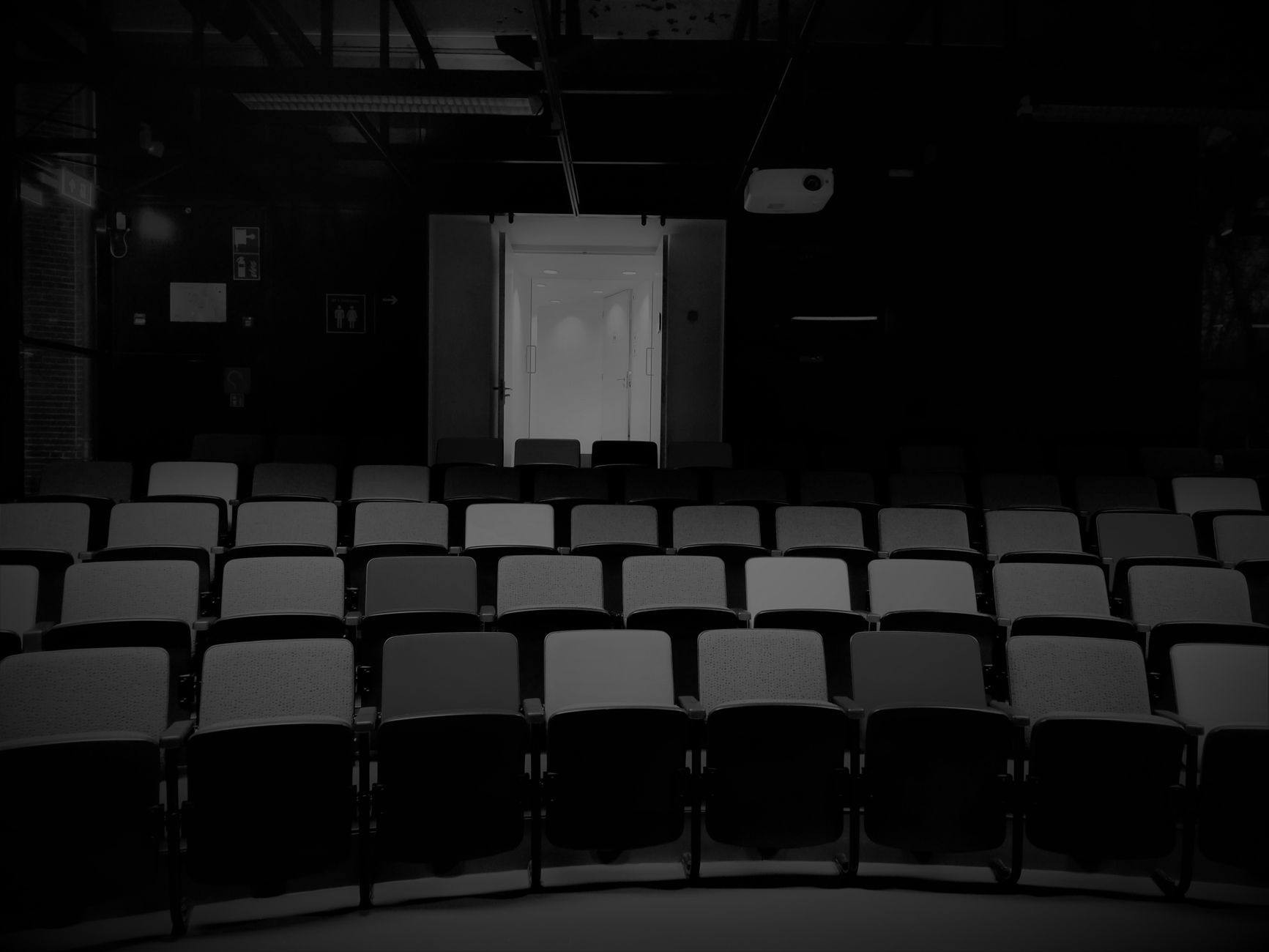 a wide-angle shot of an empty university lecture hall with feminist movement posters visible on a bulletin board near the entrance, chairs arranged in rows under fluorescent lighting