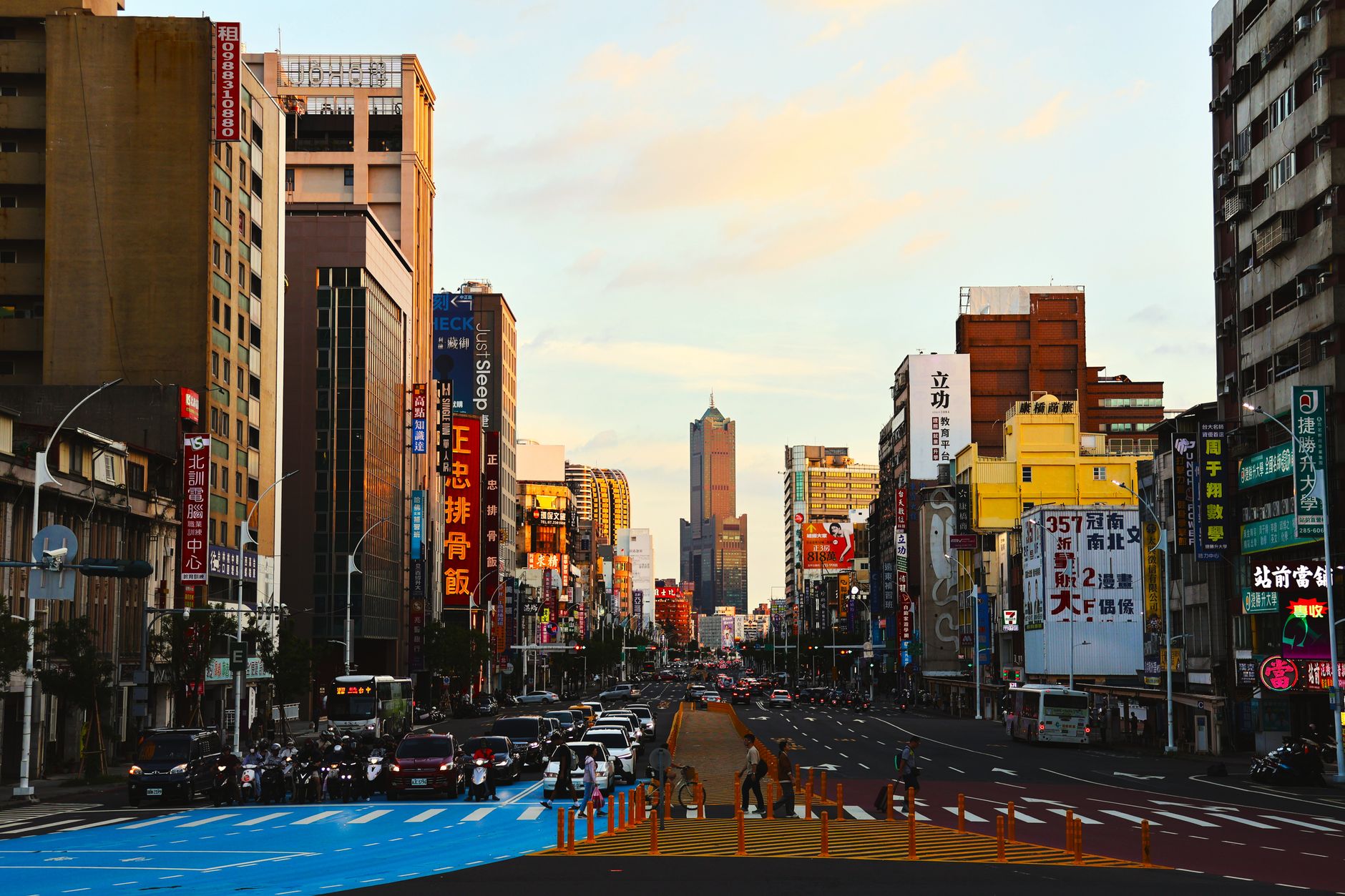 a column of M1A2 Abrams tanks staged along a wide Taiwanese urban boulevard flanked by commercial storefronts and overpasses, shot from street level with the city environment as the focal point