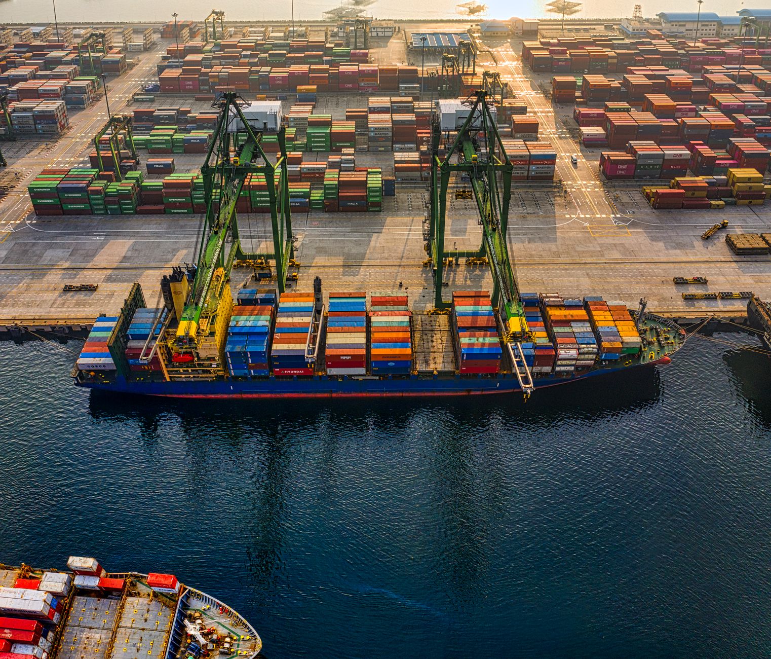 aerial view of a busy commercial shipping port with stacked cargo containers and docked container vessels, no identifying logos visible