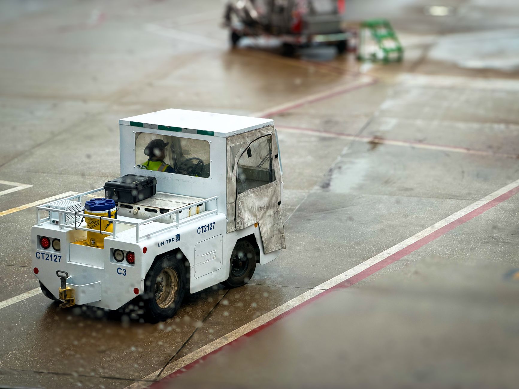 a large fixed-wing unmanned aerial vehicle on a concrete airfield apron, viewed from the side, with a ground support crew visible at a distance near a maintenance vehicle
