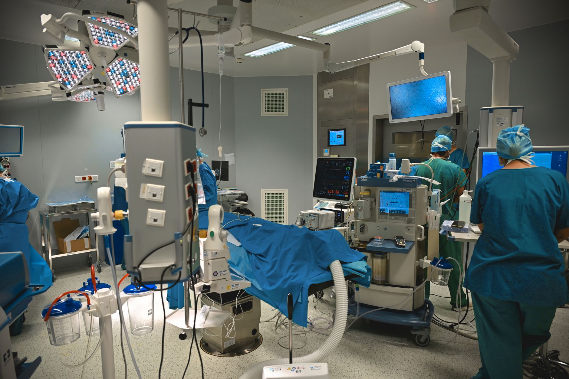 interior view of a field medical station with monitoring equipment and a folded stretcher resting against a bare concrete wall, no personnel present
