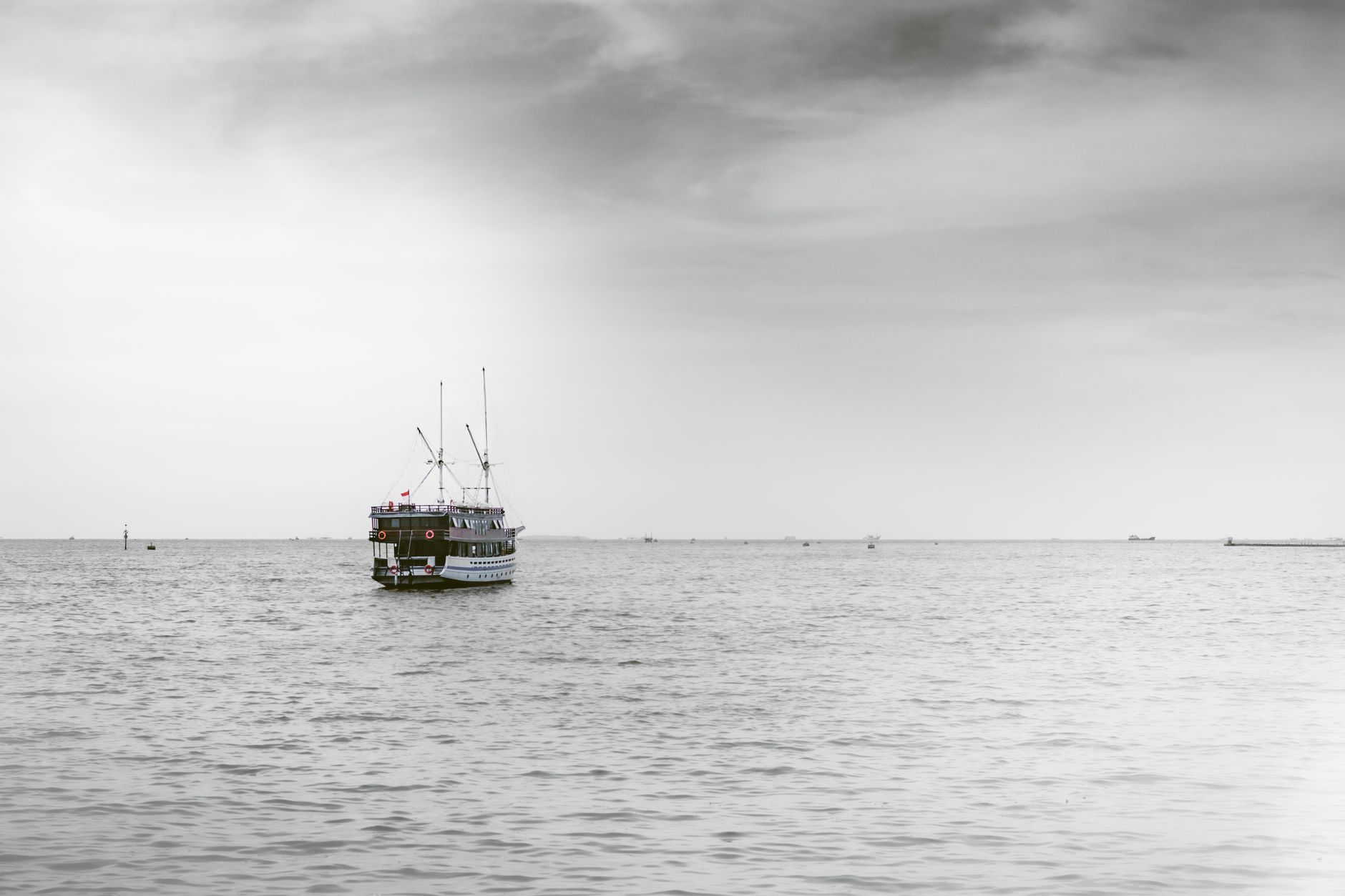 a small gray uncrewed surface vessel moving across open dark water toward a distant coastline, viewed from low altitude