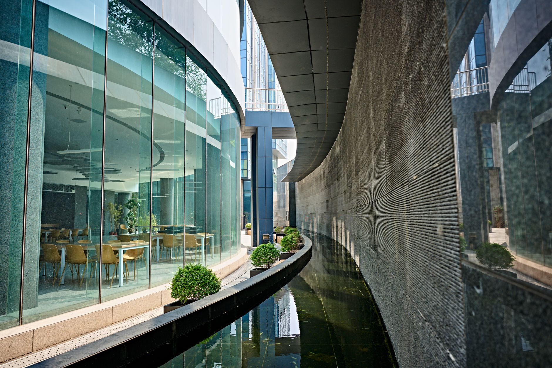 an Israeli technology campus building exterior with glass facades reflecting daylight, surrounded by landscaped grounds, viewed from across a wide pedestrian plaza