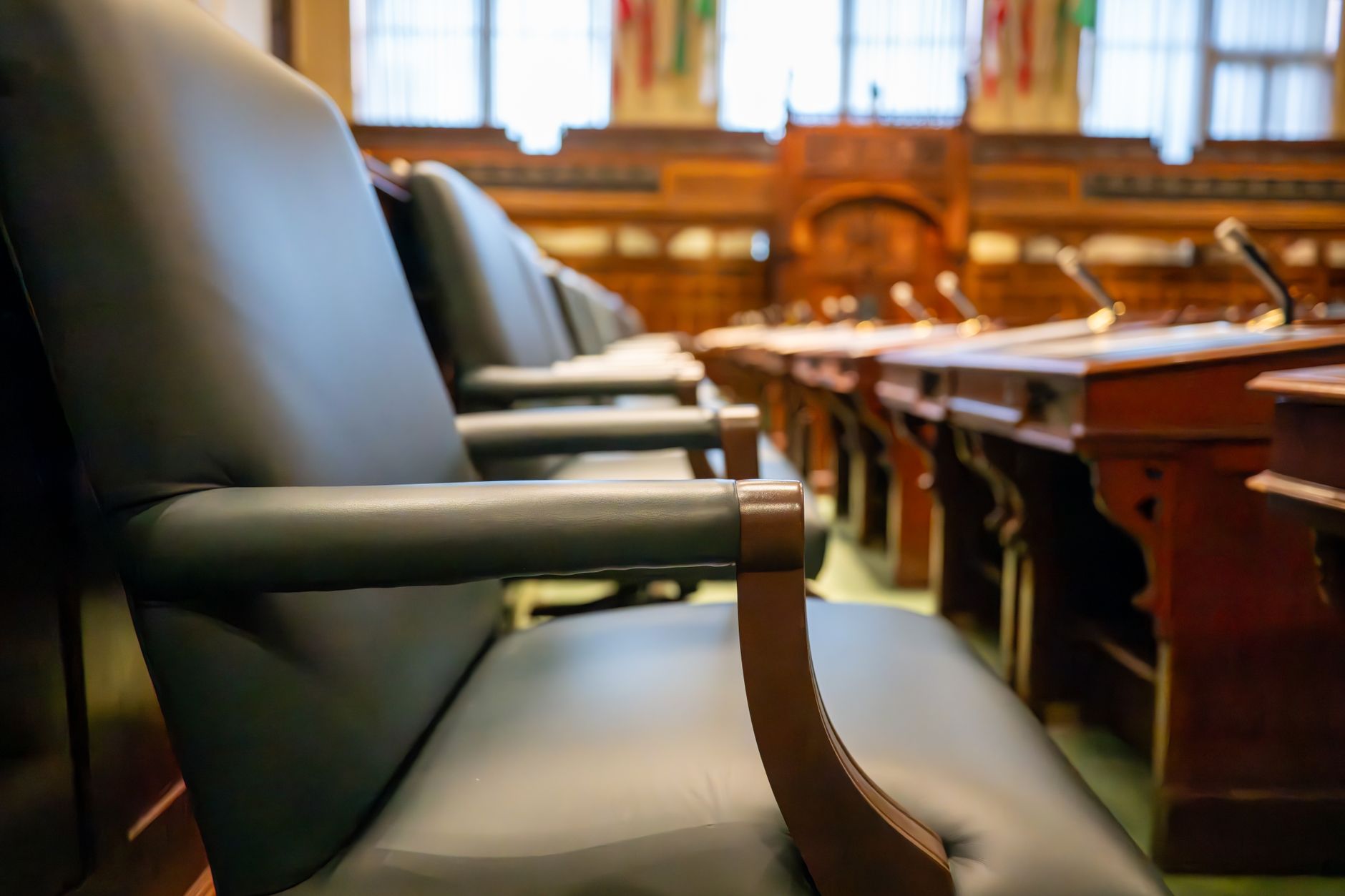 a congressional hearing room mid-session showing committee members at a curved dais with documents and screens visible, taken from the press gallery at wide angle