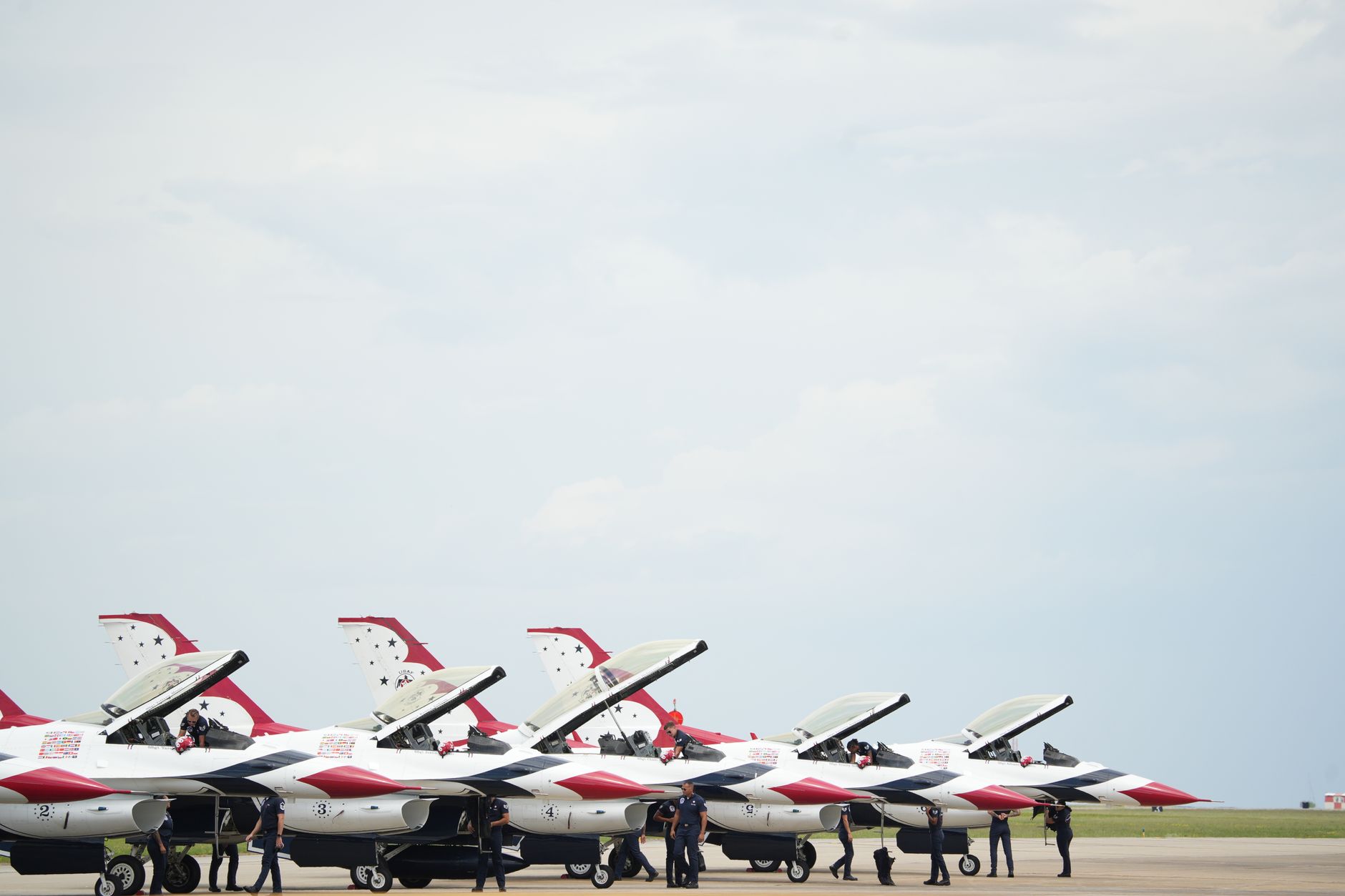 two fifth-generation jet fighters on a flight line at a NATO air base, parked side by side with ground crew visible in the distance performing pre-flight checks