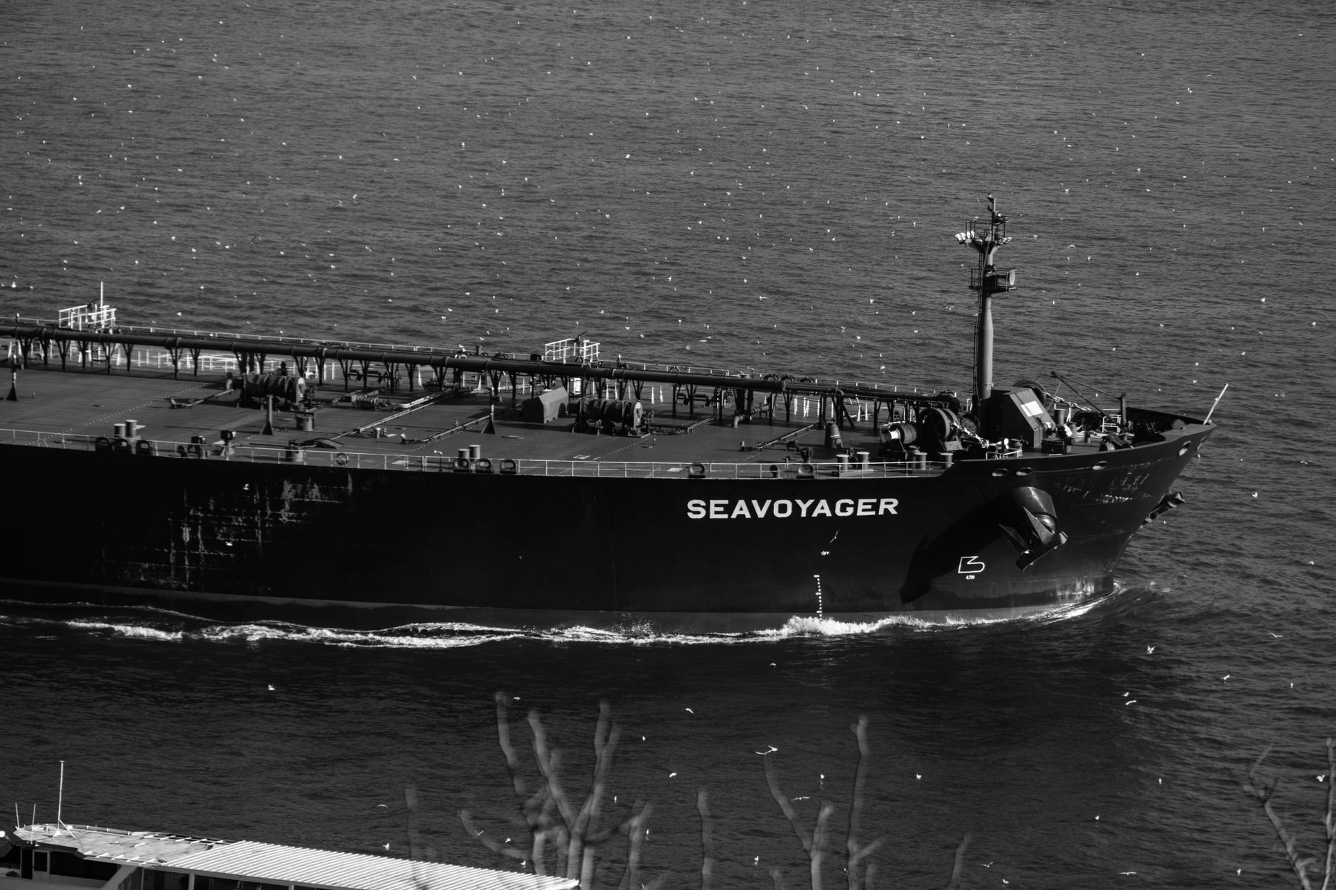 a large aircraft carrier viewed from the waterline at a commercial port, with diving maintenance equipment visible alongside the hull