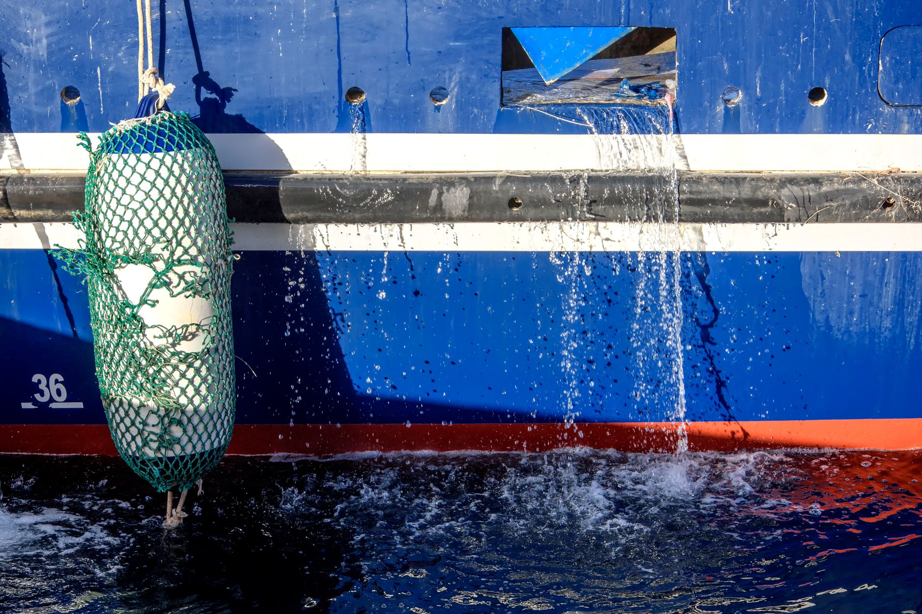 underwater view of a ship's hull with barnacle and marine growth visible, divers working with cleaning equipment in clear blue water
