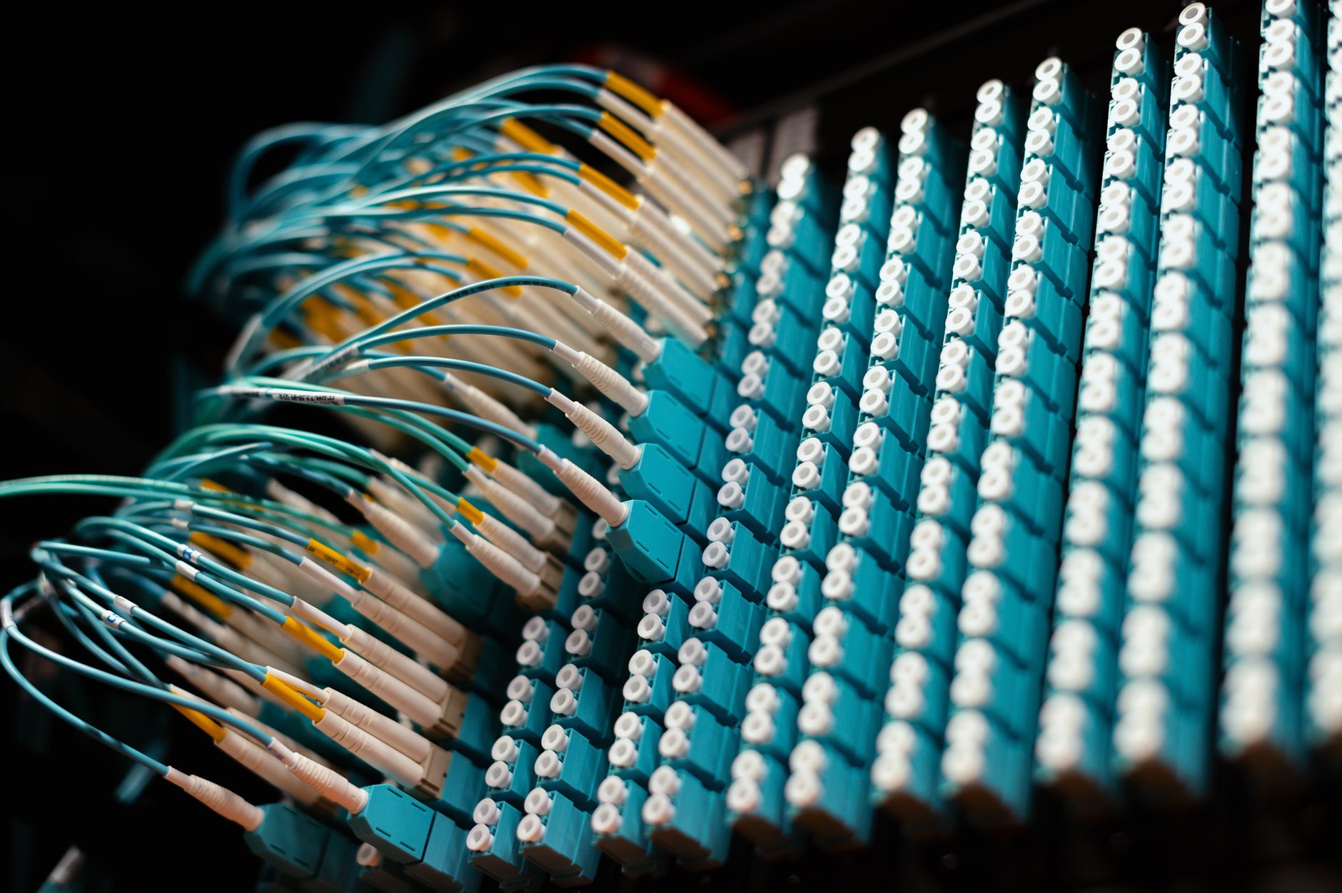 a server infrastructure room with rows of rack-mounted equipment and fiber optic cable bundles, soft blue indicator lights illuminating the aisle