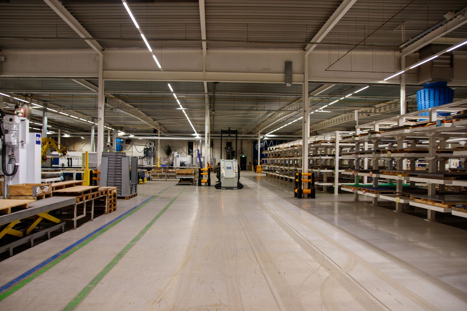 a row of compact autonomous drone units stored in charging cradles inside a clean industrial warehouse facility, shelving and control equipment visible in the background