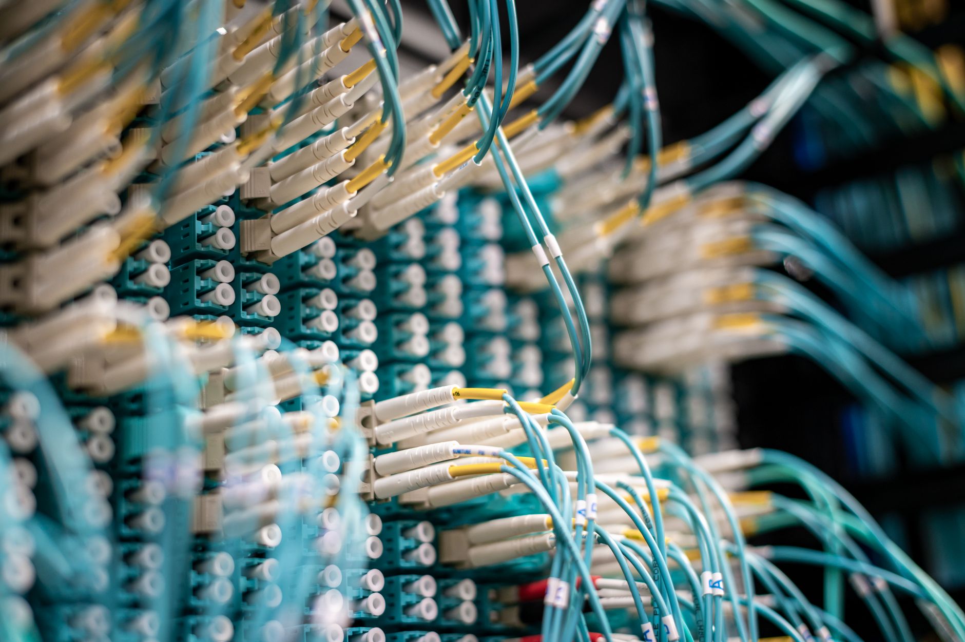 rows of server infrastructure and fiber-optic cabling inside a secure data center facility, shot from the aisle looking down the corridor