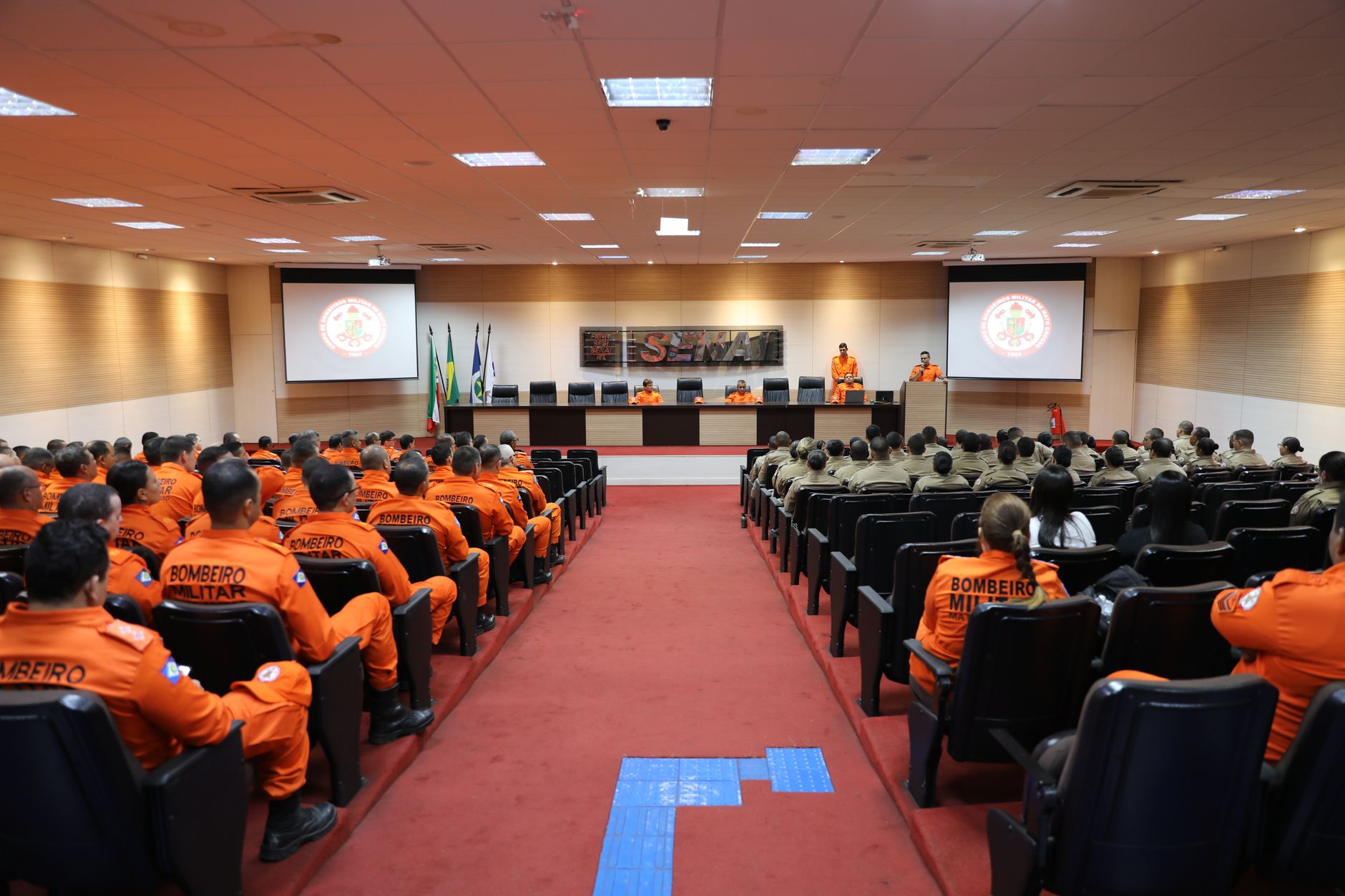 a large convention center exhibition hall with military technology displays and uniformed personnel visible in the background, wide environmental shot
