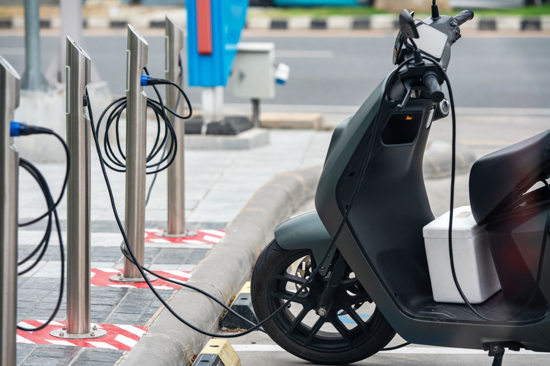 rows of electric vehicle charging stations in a large commercial parking structure, cables connected, overhead LED lighting visible
