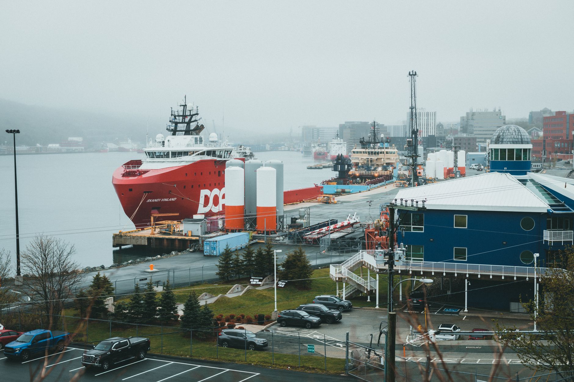 aerial view of a naval shipyard on a coastal inlet showing dry docks, covered construction halls, and moored vessels alongside industrial craneage