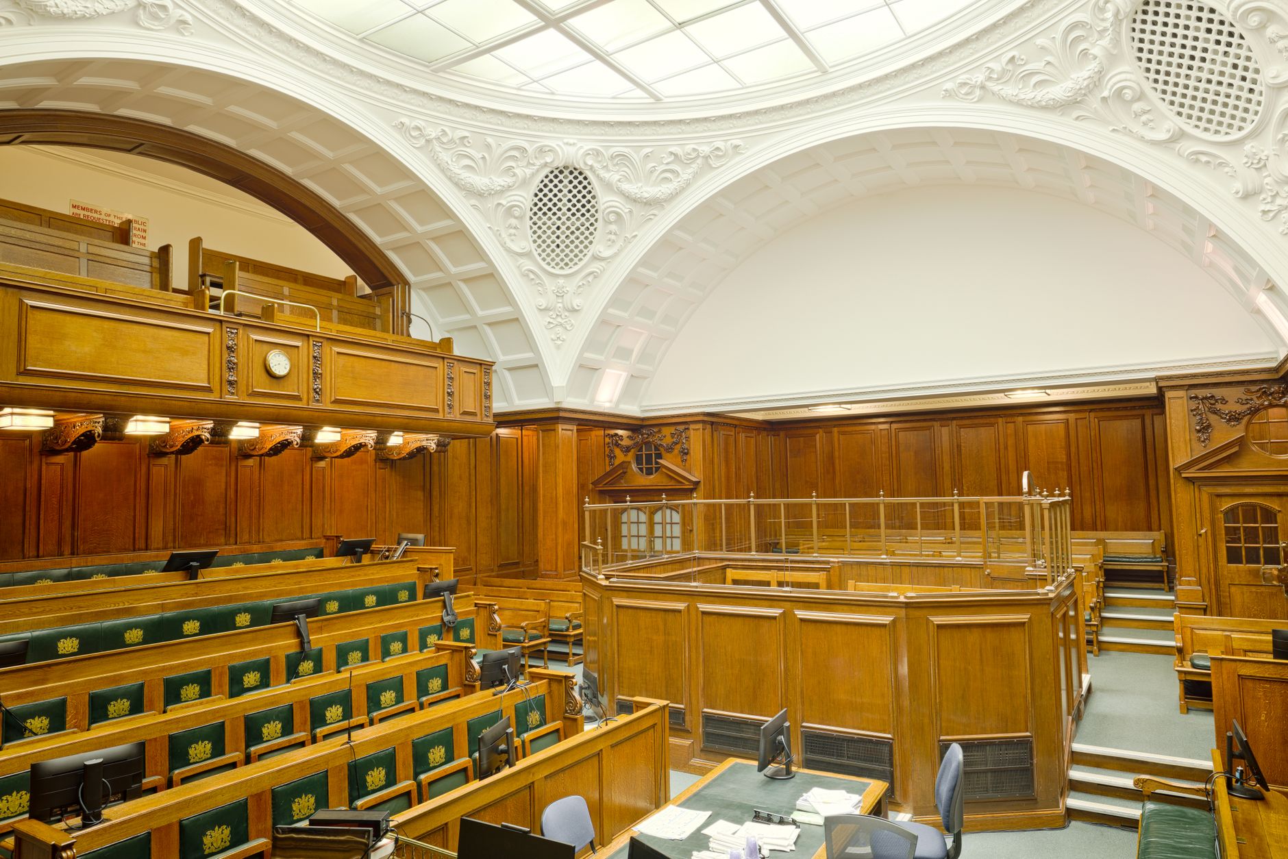 a congressional hearing room viewed from the back, empty tiered dais with microphones and name placards, overhead lighting illuminating the chamber