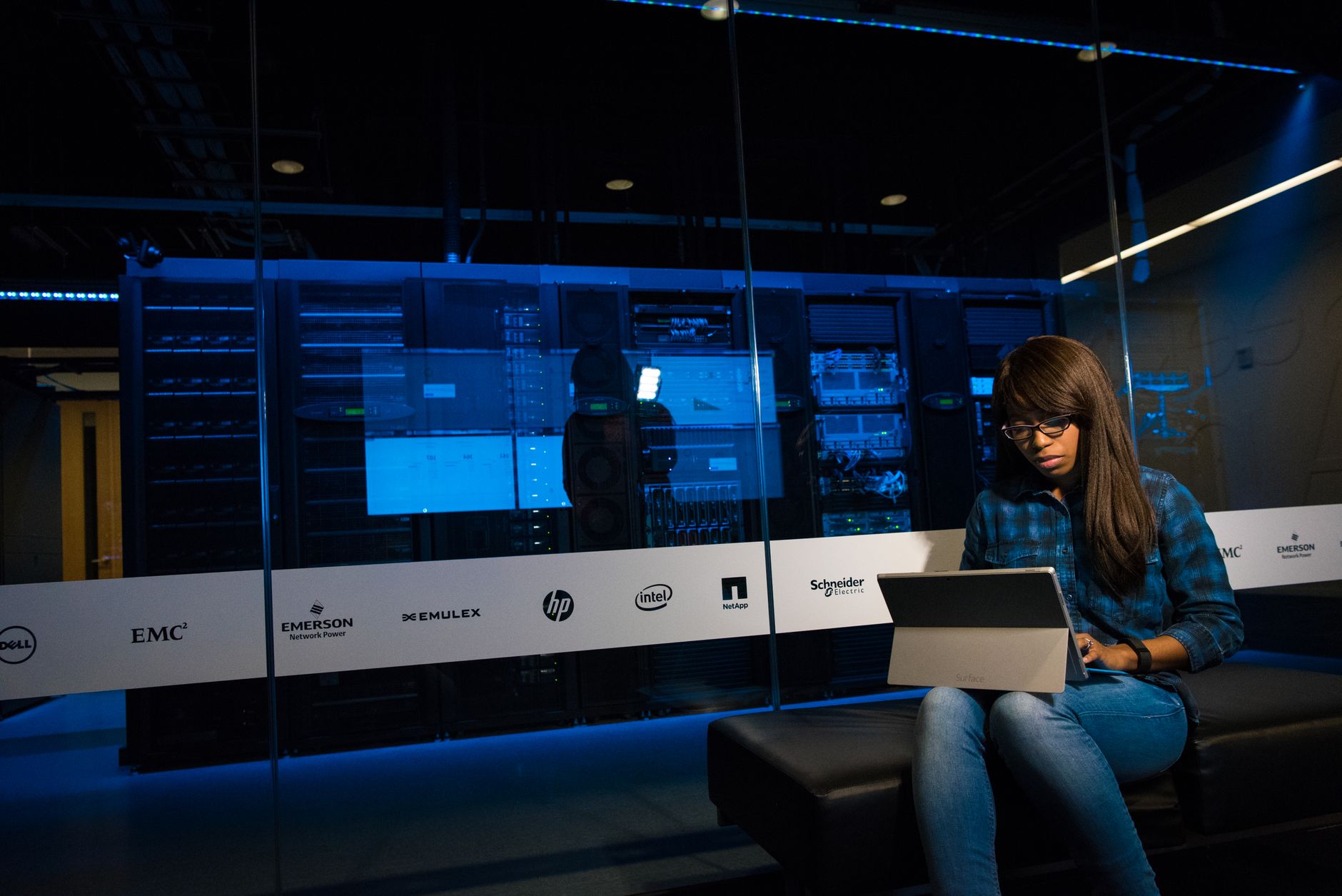 an engineer at a workstation reviewing lines of code on dual monitors in a dimly lit cybersecurity operations center, server indicators blinking in the background