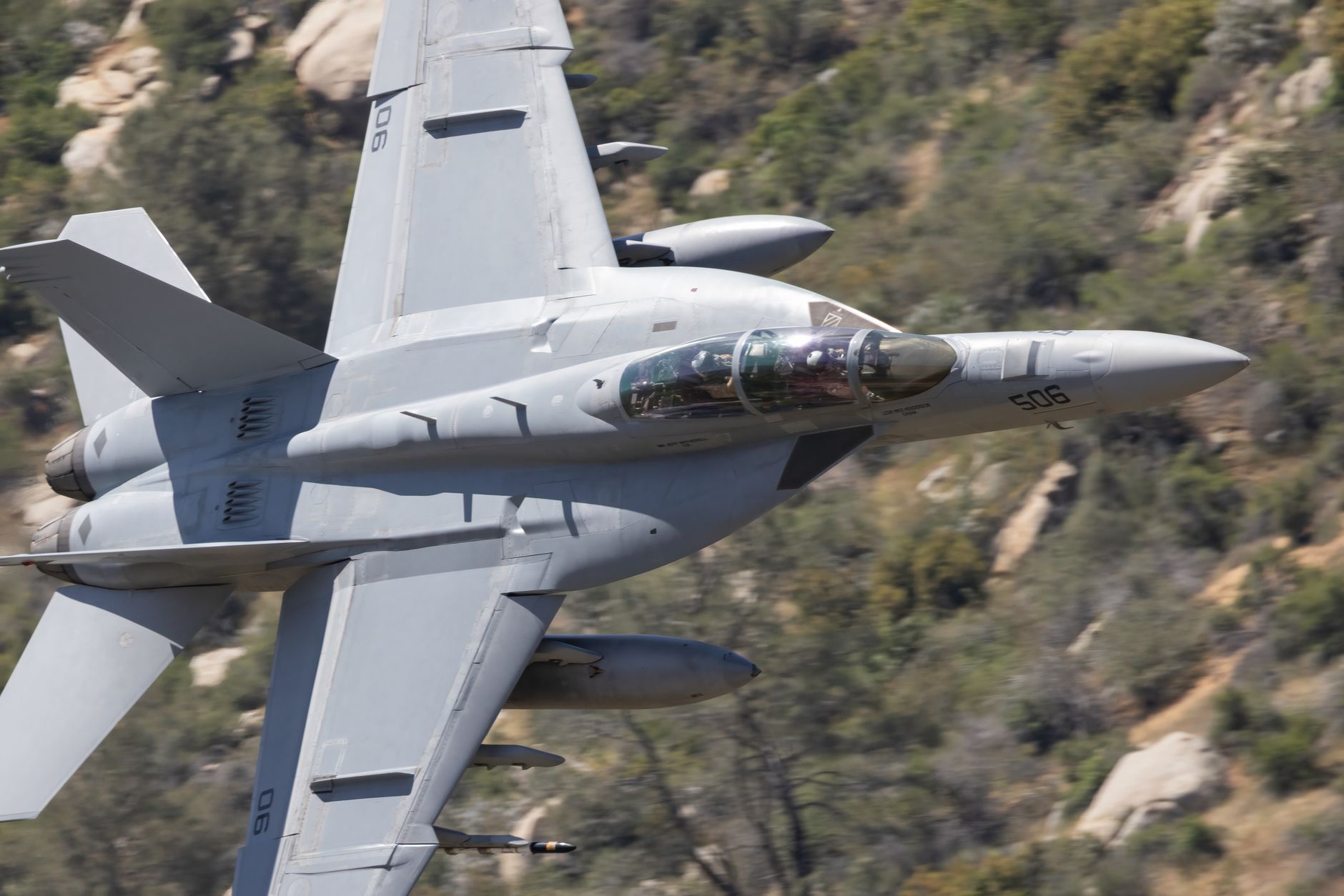 an F-15E Strike Eagle aircraft in flight over arid Australian scrubland, viewed from a chase plane, weapon pylon visible beneath the wing
