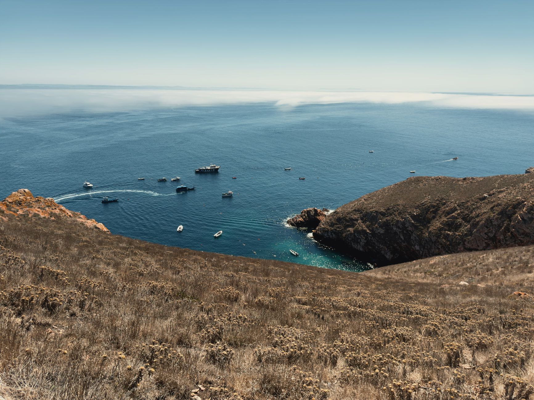 aerial view of a narrow strait coastline with rocky terrain and a naval vessel visible in calm waters below