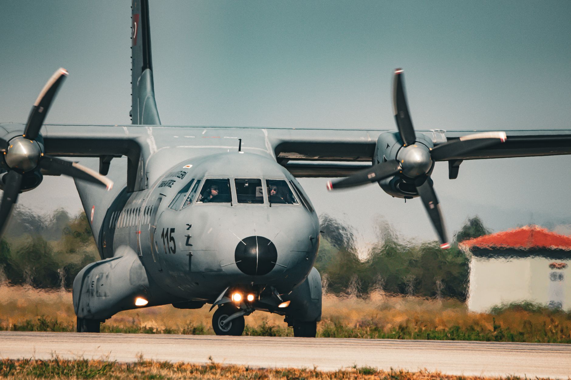 a large four-engine turboprop strategic bomber parked on a wide military airfield apron, viewed from a low angle with its swept wings and contra-rotating propellers visible against an overcast sky