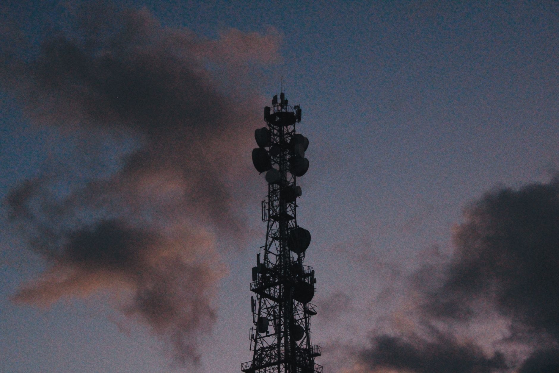 a large forward operating base in a desert environment, featuring hardened structures, vehicle staging areas, and communication antenna arrays at dusk