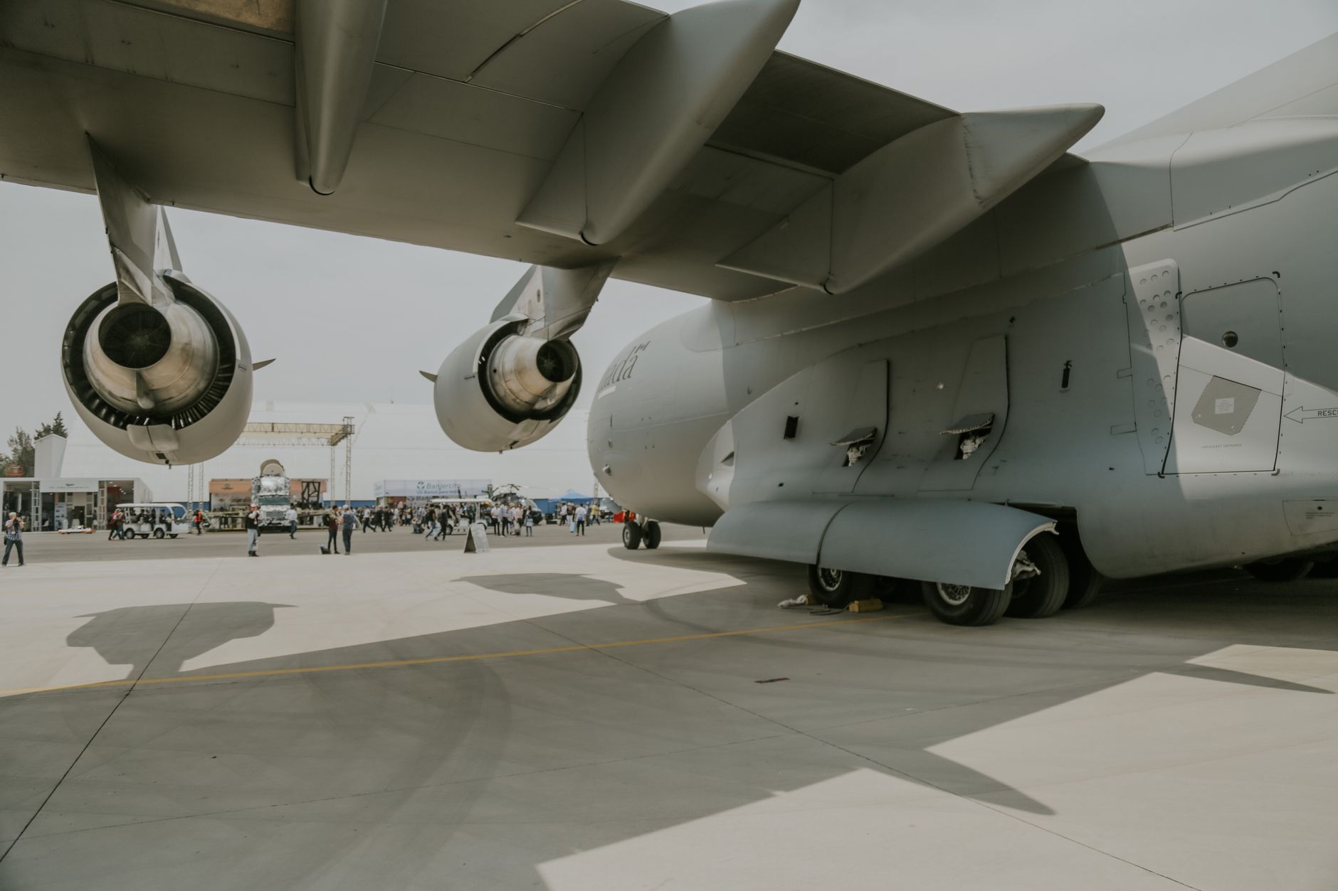 rows of military cargo transport vehicles and equipment pallets staged inside a large aircraft hangar at a desert air base, prepared for airlift operations
